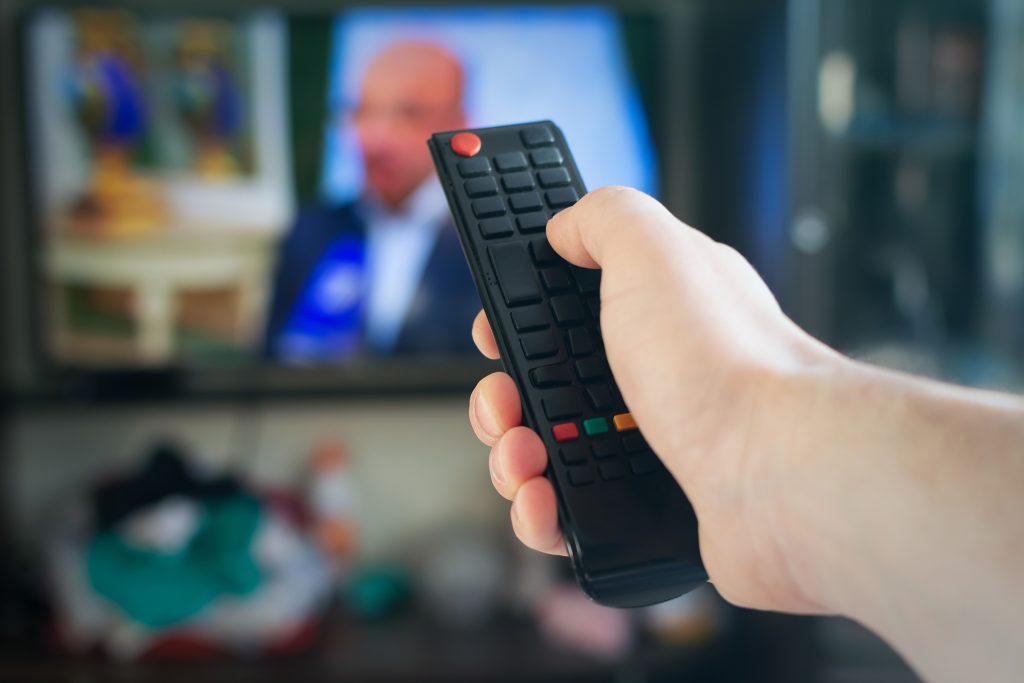 A man with a remote control in his hand switches channels on the TV.